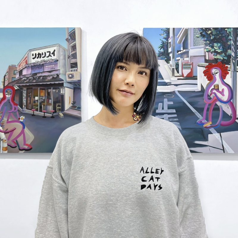 Portrait of the artist Yufi in front of two of her paintings
