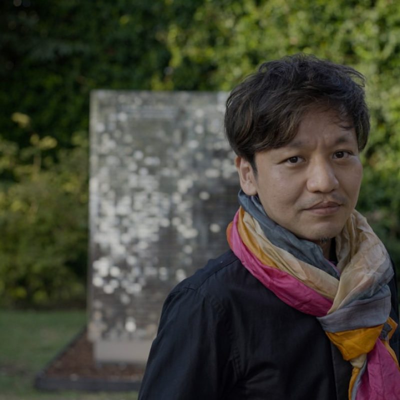 Portrait of the artist Kaz Shirane beside one of his mirror works